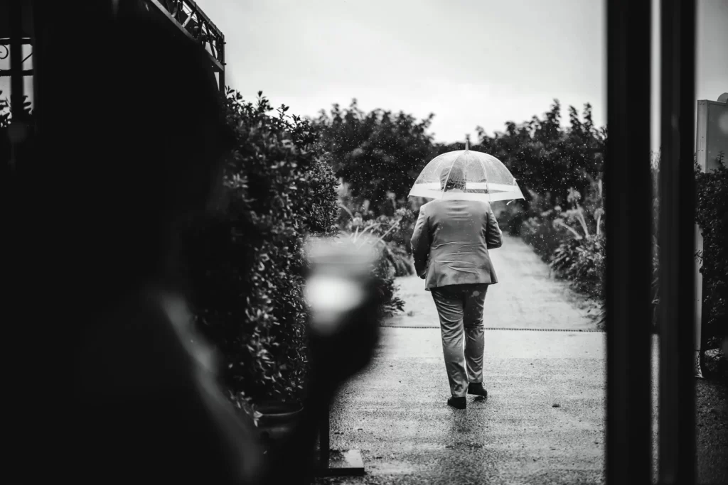 Photo noir et blanc d'un marié sous la pluie avec un parapluie