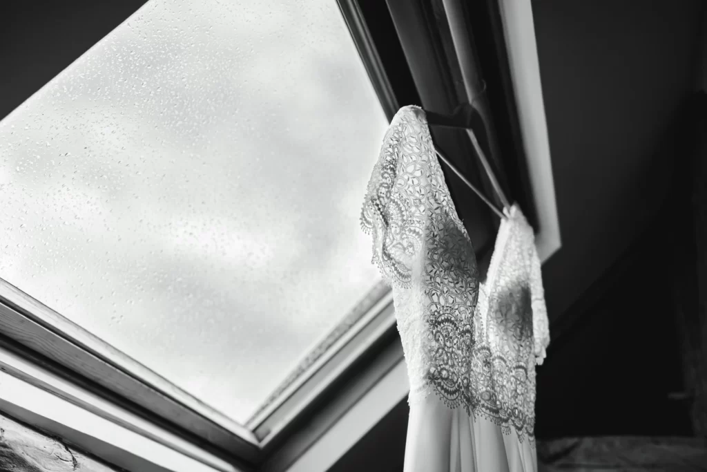 cintre mariage soutenant une robe de mariée sous un velux avec des gouttes de pluie