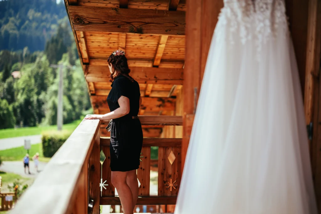 Photo de la future mariée sur un balcon de son chalet, près de sa robe de mariée pendant sa préparation